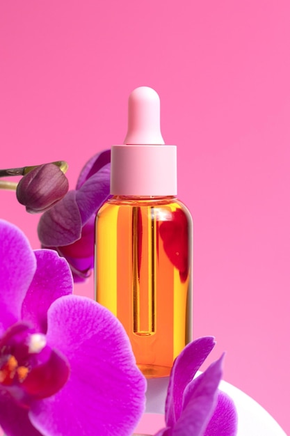 Modell einer Glasflasche auf rosa Hintergrund Rosafarbene Orchideenblüten befinden sich neben Blasen mit Öl