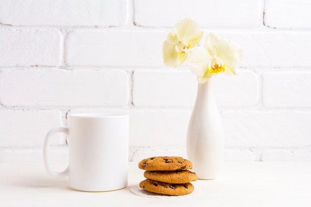 Modell einer weißen Kaffeetasse mit sanfter gelber Orchidee in Vase und Keksen