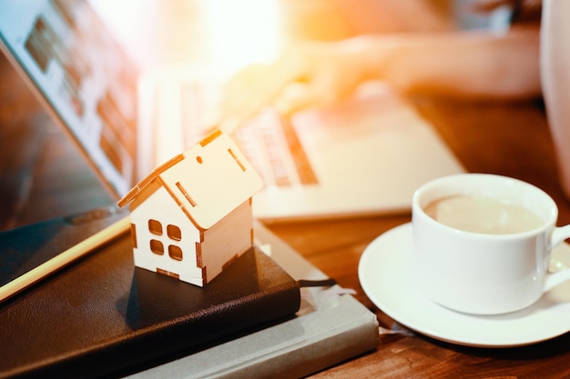 Modell eines Holzhauses auf dem Hintergrund eines LaptopsKonzept der Immobiliensuche im InternetKauf oder Versicherung von Wohnungen
