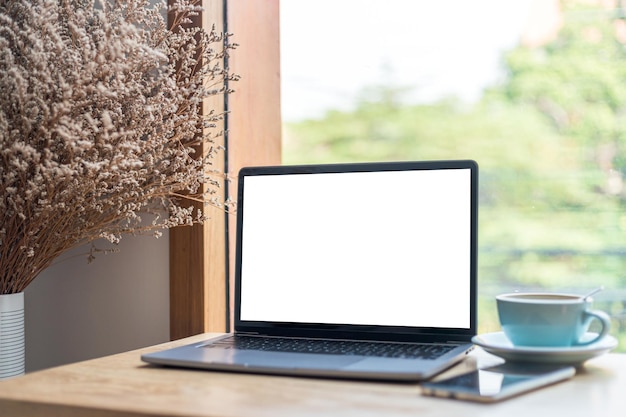 Modell eines Laptop-Computers mit leerem Bildschirm mit Kaffeetasse und Smartphone auf dem Tisch des Café-Hintergrunds, weißer Bildschirm