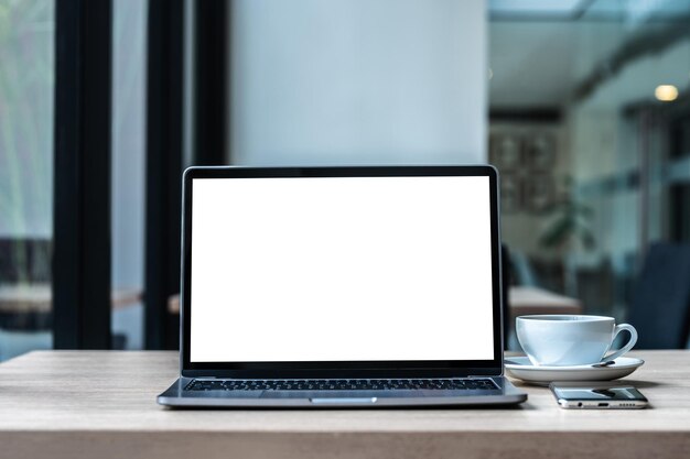 Modell eines Laptop-Computers mit leerem Bildschirm mit Kaffeetasse und Smartphone auf dem Tisch des Café-Hintergrunds Weißer Bildschirm