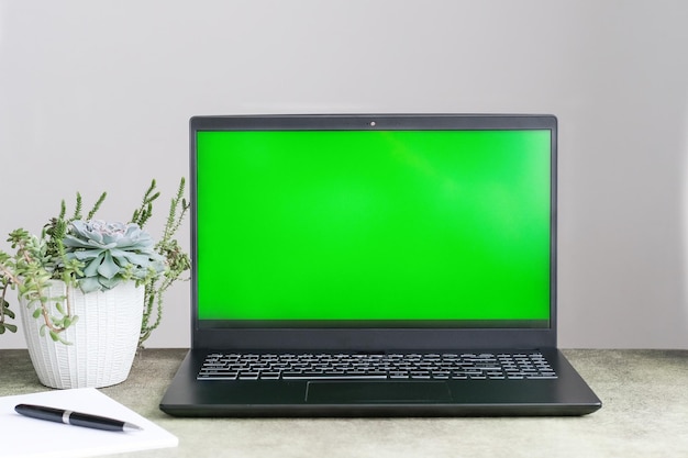 Modell eines Laptop-Computers mit leerem grünen Bildschirm auf dem Tisch