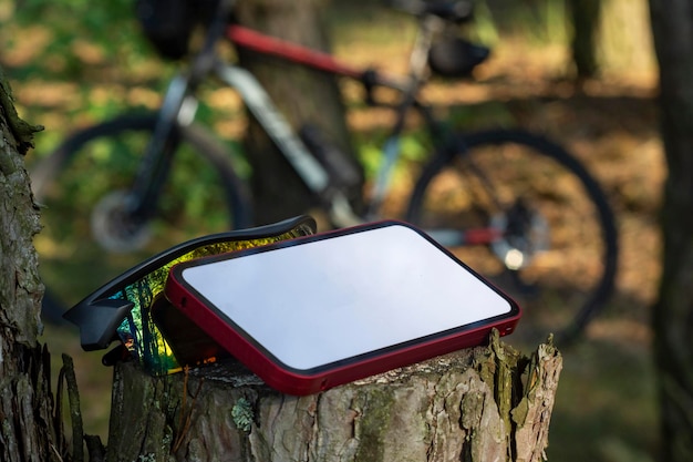 Modell eines Smartphones mit weißem Display im Wald vor dem Hintergrund eines Mountainbikes