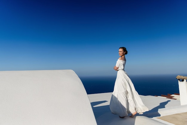 Modell im weißen Kleid, das glücklich die Sonne genießt und auf den blauen Himmel blickt. Ein schönes Mädchen in einem weißen Kleid