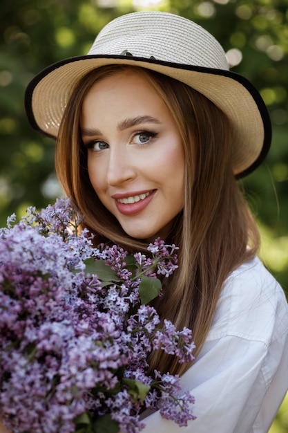 Modell mit blauen Augen in einem Sommerhut mit einem Blumenstrauß in einem Sommerpark für einen Spaziergang. großes Porträt. Lächeln und Glück. Romantik