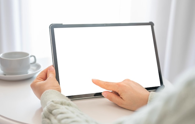 Modell-Tablet Frauen-Hand-Touch-Tablet mit leerem, leerem Bildschirm Frau sitzt am runden weißen Tisch und hält Modell-Tablet mit weißem, leerem Bildschirm High Key