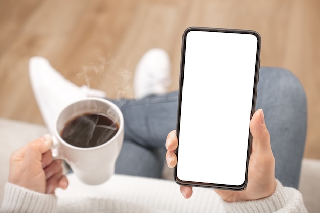 Modellbild der Frau, die schwarzes Handy mit leerem weißen Bildschirm im Café hält.