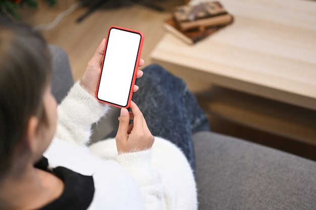 Modellbild der Frauenhand, die mobiles Telefon auf Sofa zu Hause hält. Leerer Bildschirm für Werbetext.