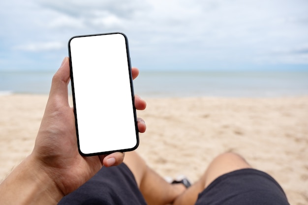 Modellbild der Hand eines Mannes, der ein schwarzes Mobiltelefon mit leerem Desktop-Bildschirm hält, während er sich auf den Strandkorb legt