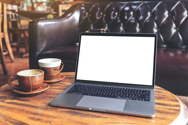 Modellbild des Laptops mit leerem weißen Desktop-Bildschirm und Kaffeetasse auf Holztisch im Café