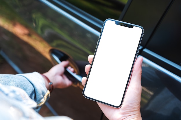 Modellbild einer Frau, die ein Mobiltelefon mit leerem Bildschirm hält und benutzt, während sie die Autotür öffnet