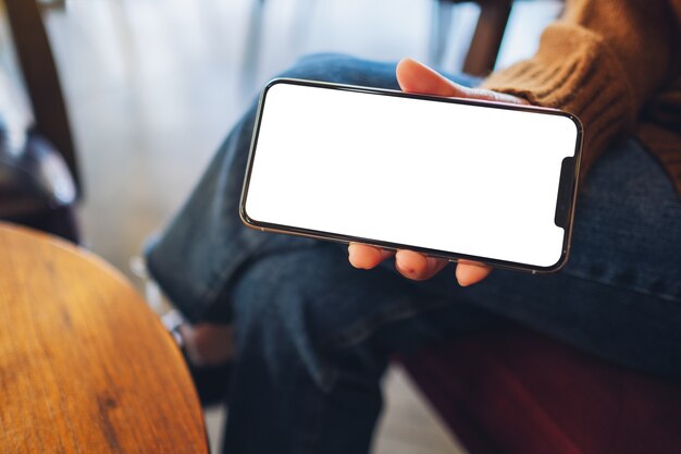 Modellbild einer Frau, die ein schwarzes Handy mit leerem Bildschirm im Café hält und zeigt