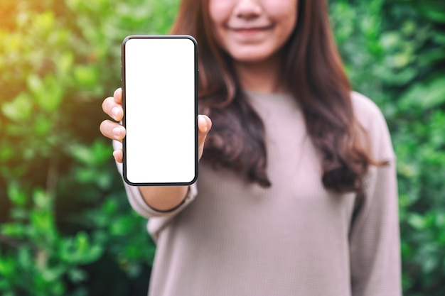 Modellbild einer Frau, die ein schwarzes Handy mit leerem Bildschirm mit grünem Naturhintergrund hält und zeigt