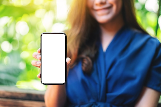 Modellbild einer Frau, die ein schwarzes Handy mit leerem Bildschirm mit grünem Naturhintergrund hält und zeigt