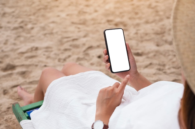 Modellbild einer Frau, die ein schwarzes Handy mit leerem Desktop-Bildschirm hält, während sie auf einem Strandkorb sitzt