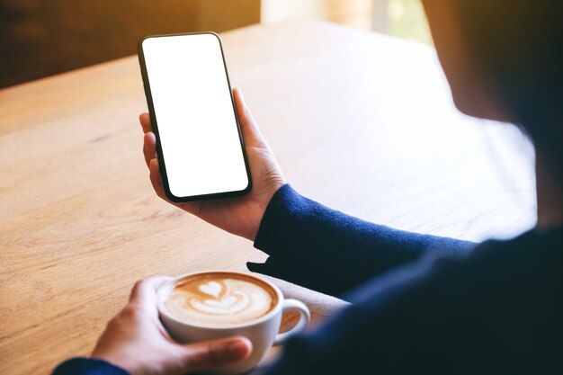 Modellbild einer Frau, die ein weißes Handy mit leerem Bildschirm hält, während sie Kaffee trinkt