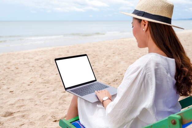 Modellbild einer Frau, die einen Laptop mit leerem Desktop-Bildschirm verwendet und tippt, während sie auf einem Strandkorb sitzt