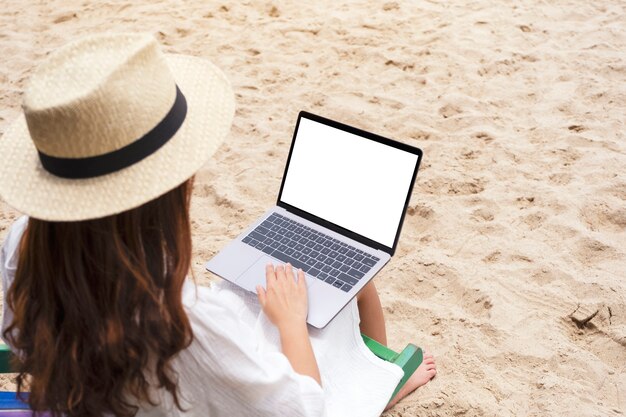 Modellbild einer Frau, die einen Laptop mit leerem Desktop-Bildschirm verwendet und tippt, während sie auf einem Strandkorb sitzt
