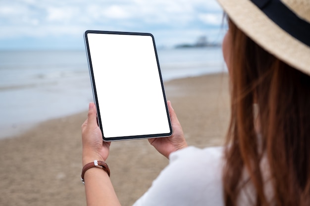 Modellbild einer Frau, die einen schwarzen Tablet-PC mit leerem Desktop-Bildschirm am Meer hält