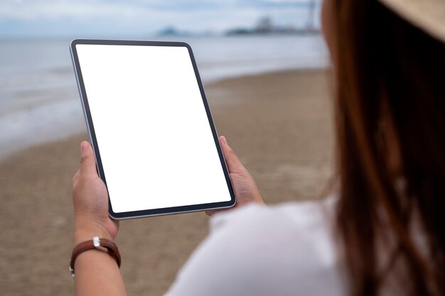 Modellbild einer Frau, die einen schwarzen Tablet-PC mit leerem Desktop-Bildschirm am Meer hält