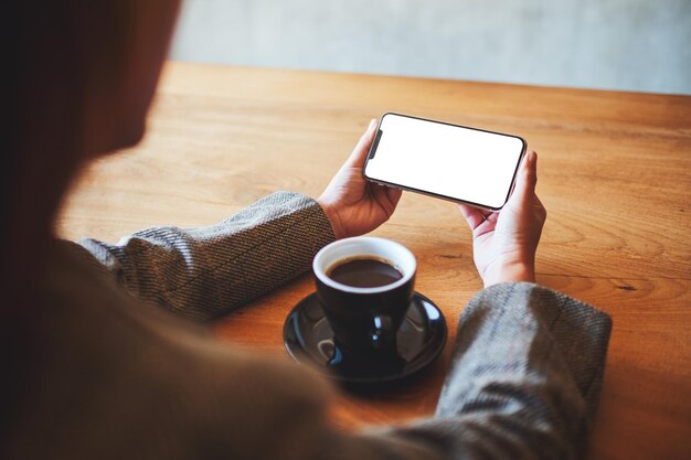 Modellbild einer Frau, die Handy mit leerem Bildschirm mit Kaffeetasse auf Holztisch hält