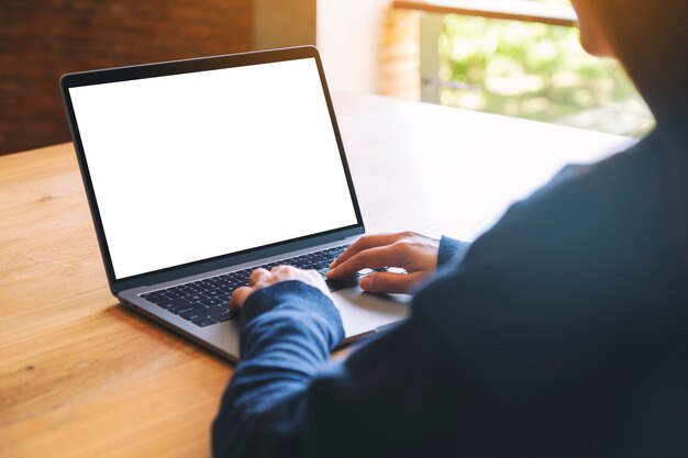 Modellbild einer Frau, die Laptop-Computer-Tastatur mit leerem weißem Desktop-Bildschirm auf Holztisch verwendet und tippt