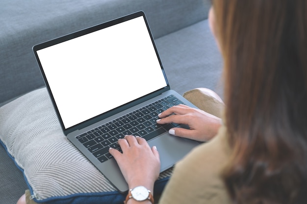 Modellbild einer Frau, die Laptop-Tastatur mit leerem weißen Bildschirm beim Sitzen im Wohnzimmer verwendet und tippt