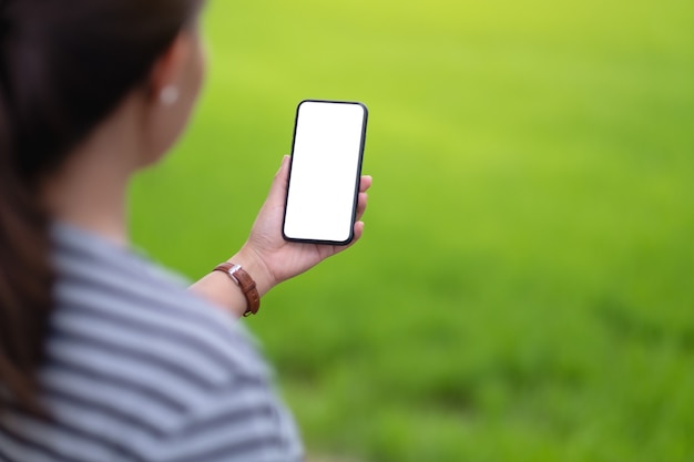 Modellbild einer Frau, die schwarzes Handy mit leerem Desktop-Bildschirm mit unscharfem grünem Naturhintergrund hält