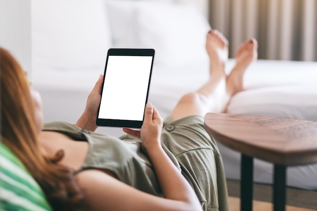 Modellbild einer Frau, die Tablet-PC mit leerem Bildschirm hält und verwendet, während sie sich entspannt und auf dem Bett liegt