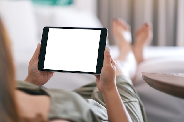 Modellbild einer Frau, die Tablet-PC mit leerem Bildschirm horizontal hält und verwendet, während sie sich entspannt und auf dem Bett liegt