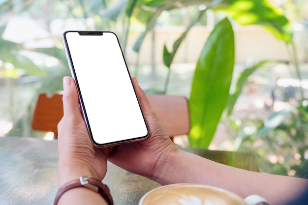 Modellbild einer Frau mit schwarzem Handy mit leerem Bildschirm mit Kaffeetasse auf Holztisch