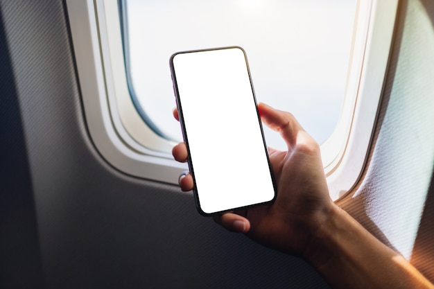 Modellbild einer Hand, die ein schwarzes Mobiltelefon mit leerem Desktop-Bildschirm neben einem Flugzeugfenster hält