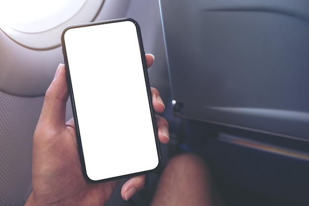 Modellbild einer Hand, die ein schwarzes Smartphone mit leerem Desktop-Bildschirm neben einem Flugzeugfenster hält