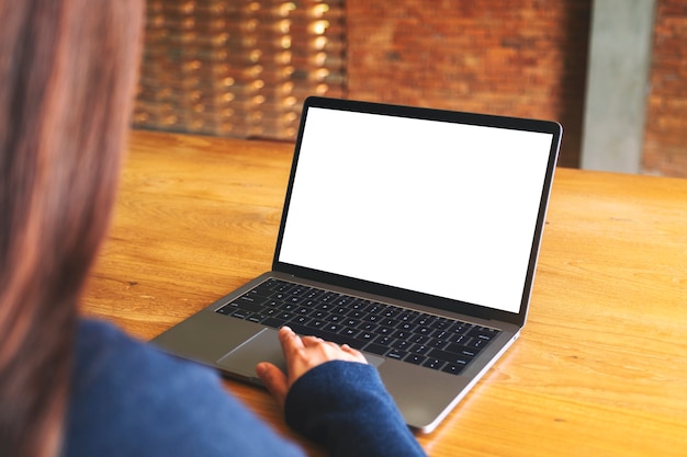 Modellbild einer Hand, die Laptop-Touchpad mit leerem weißem Desktop-Bildschirm auf Holztisch verwendet und berührt