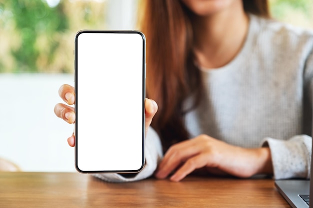 Modellbild einer schönen Frau, die ein Mobiltelefon mit leerem weißen Bildschirm hält und zeigt