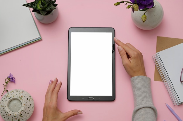 Modellbild von den Händen, die Tablet-PC auf rosa Schreibtisch halten.