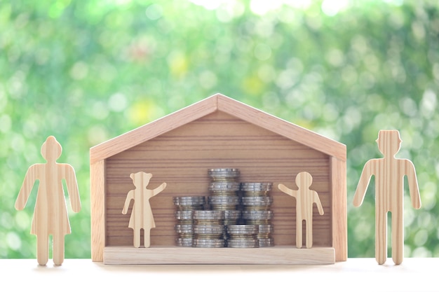 Modellfamilie und Stapel Münzgeld im Modellhaus auf natürlichem grünem Hintergrund