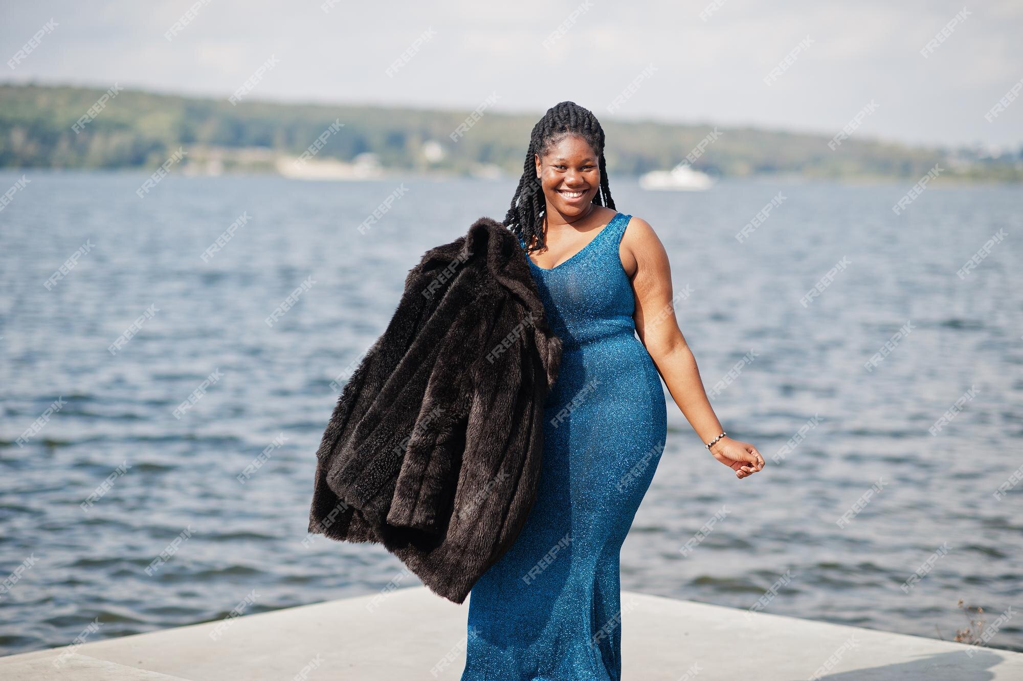 Modelo afroamericano de piel oscura de talla grande posado con un vestido azul brillante y un abrigo de piel negro contra el mar | Foto Premium Modelo afroamericano de piel oscura de talla grande posado con un vestido azul brillante y un abrigo de piel negro contra el mar | Foto Premium