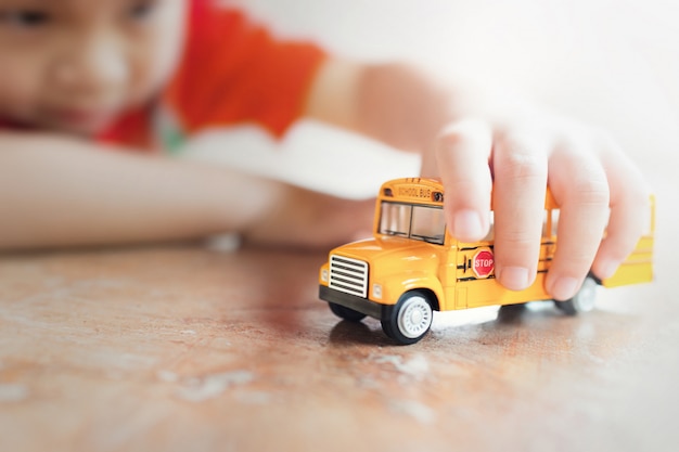 Modelo amarillo del juguete del autobús escolar en la mano del niño. Profundidad baja de la composición del campo.