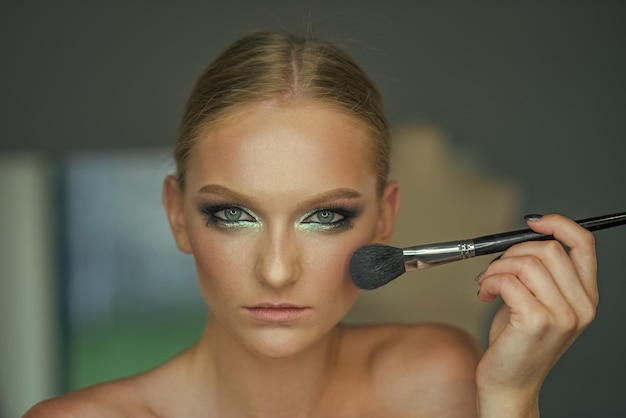 El modelo de belleza aplica polvos en la cara, cosméticos. Pincel de uso de mujer para maquillaje, rostro. Piel de niña, cuidado de la piel, cosméticos. Mujer con piel de rostro joven en salón de belleza. Curso de rostro y maquillaje glamour