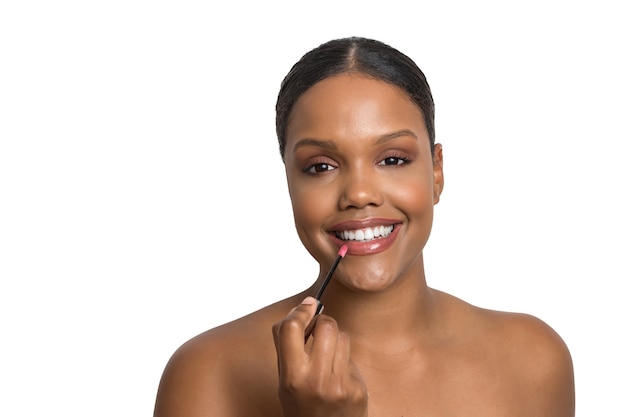 Modelo de belleza joven con piel impecable y suave sonriendo aplicando lápiz labial en una pared blanca