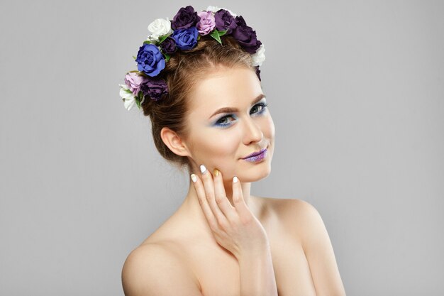 Modelo de belleza de moda chica con flores en el pelo tocando la mejilla. Maquillaje creativo perfecto y peinado de arte floral.