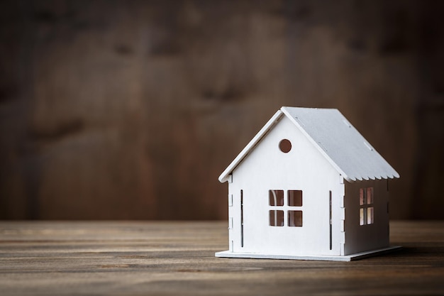 Foto modelo branco de uma casa com telhado de triângulo em um fundo de madeira marrom. conceito de propriedade imobiliária
