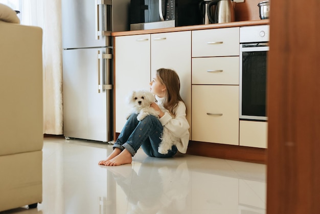 modelo brinca com cachorro branco de estimação menina da escola maltesa em casa estilo de vida na cozinha bege