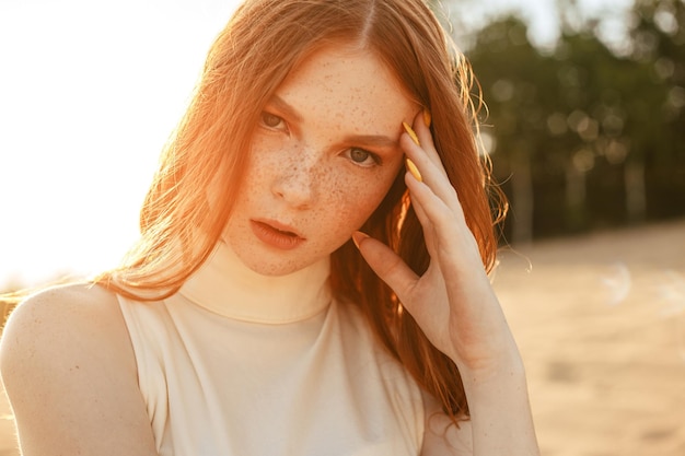 modelo con cabello pelirrojo y belleza natural tocando la cara con pecas y mirando a la cámara