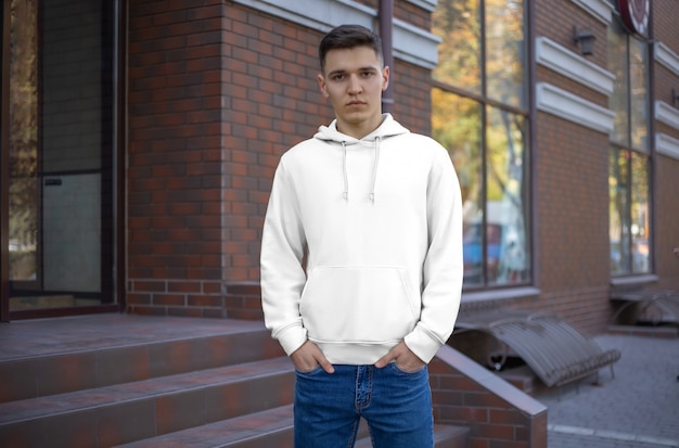 Modelo capuz masculino branco em um cara, vista frontal, apresentação de roupas na rua. capuzes de maquete no fundo de um prédio de tijolos. lugar para seu padrão e design.