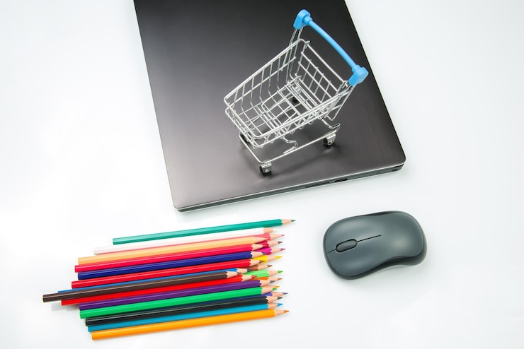 Foto modelo de carro de supermercado en el fondo de una computadora portátil con lápices de colores