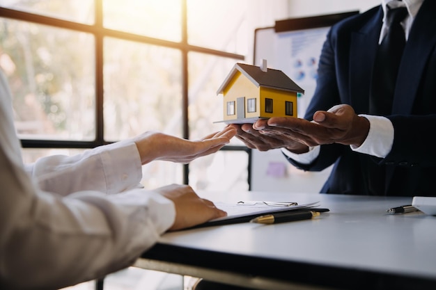 Foto modelo de casa con agente de bienes raíces y cliente discutiendo por contrato para comprar seguro de casa o fondo de préstamo de bienes raíces