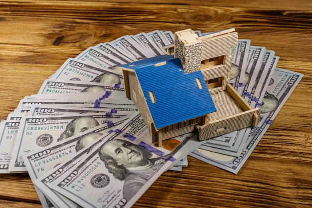 Modelo de casa y billetes de cien dólares estadounidenses sobre fondo de madera Inversión inmobiliaria préstamo hipotecario hipoteca inmobiliaria concepto