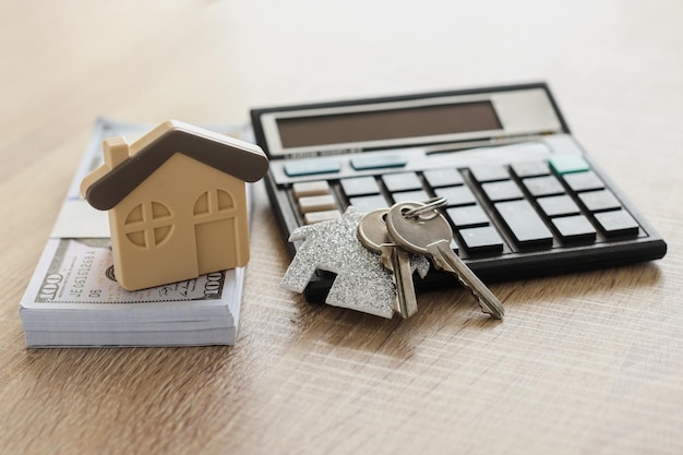 Foto modelo de casa con calculadora, dinero y llave en mesa de madera. concepto de bienes raíces.